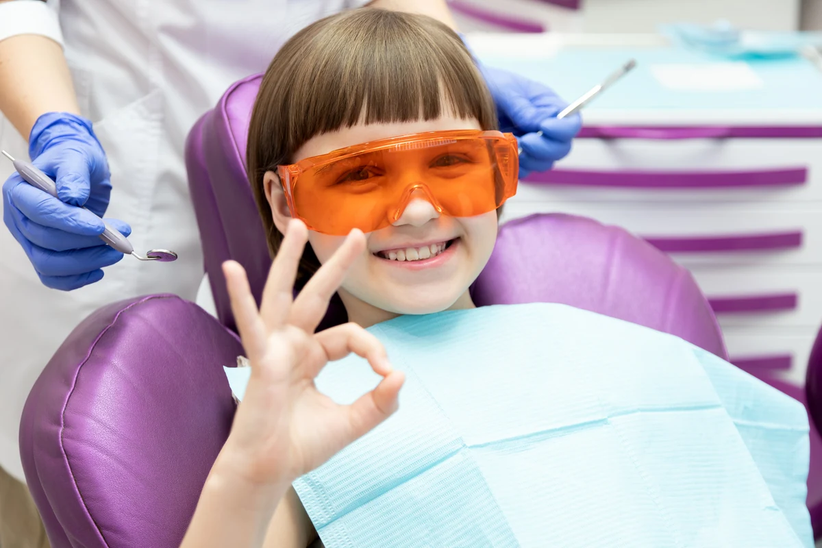 Happy child at a pediatric dental visit in Bloomingdale, IL -- smiling patient giving okay sign during dental exam at Serenity Dental